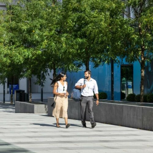 Two young professionals walking in a sunny urban environment