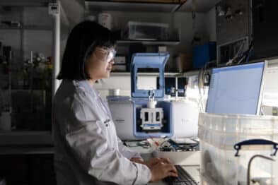 Image of researcher in white lab coat working at a lab bench.
